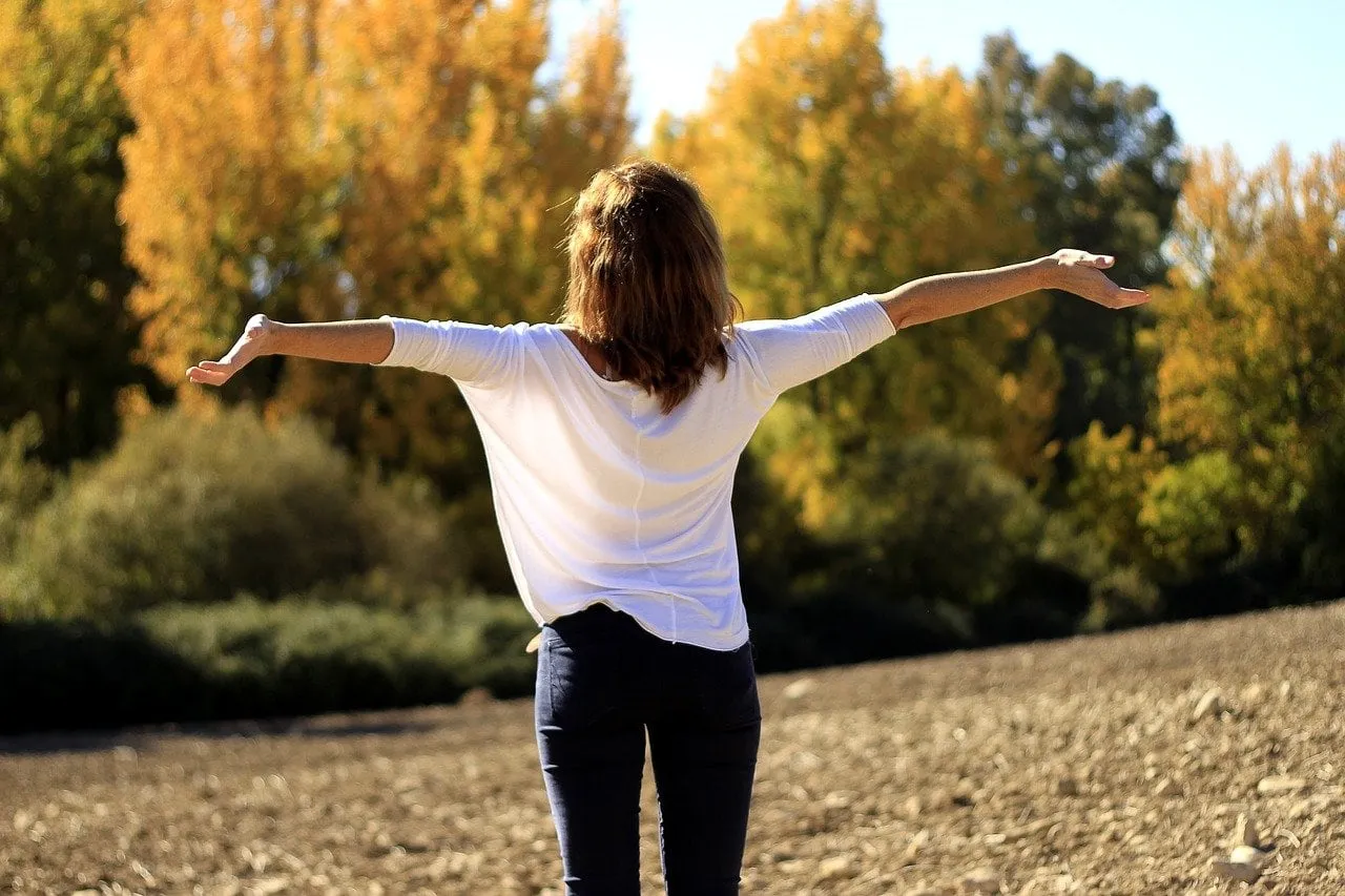 Woman standing in open field with arms outstretched, symbolizing freedom, relief, and emotional release from anxiety and everyday stressors