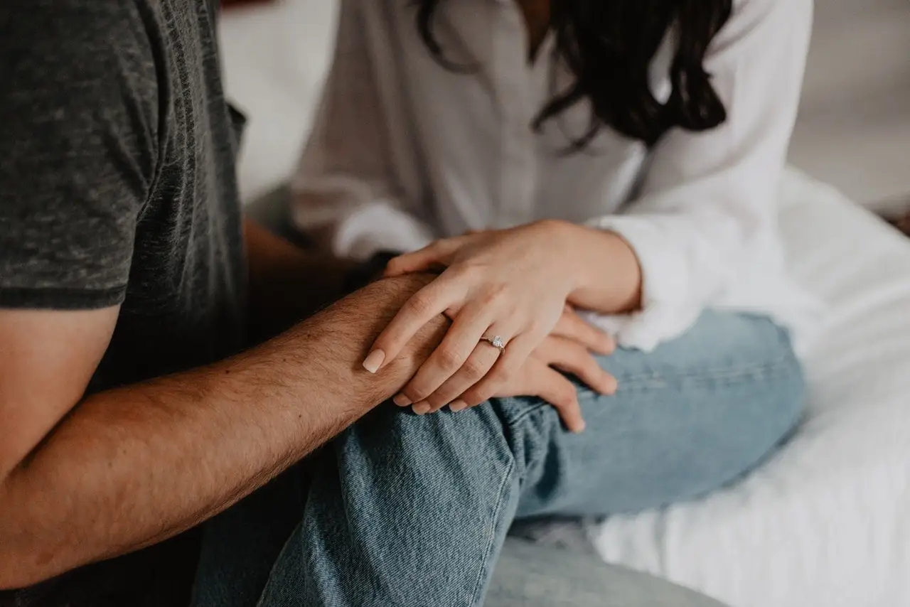 Close-up of a couple holding hands on a bed, symbolizing emotional connection, trust, and healing through relationship and couples counseling