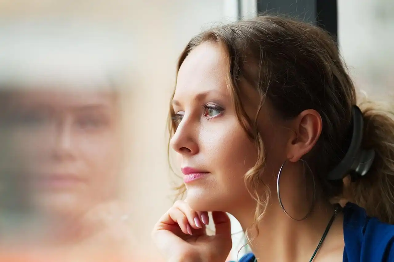 Woman gazing out a window with reflection visible, symbolizing introspection, emotional healing, and the journey through trauma with Somatic Experiencing therapy