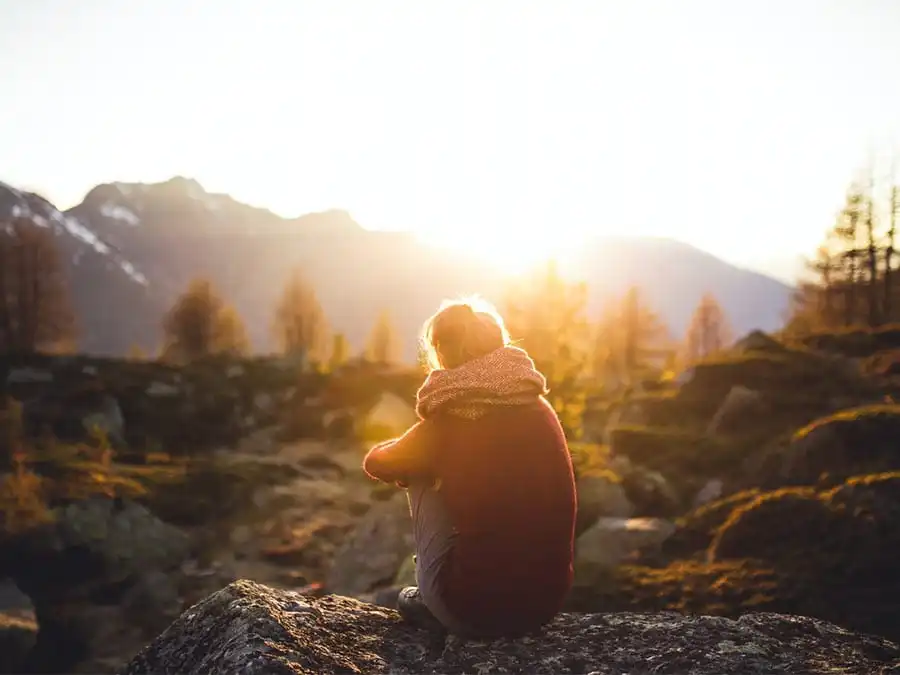 Person sitting alone on a mountain at sunrise, symbolizing reflection and healing from everyday trauma through therapy
